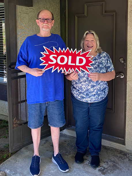 elderly couple holding sold sign